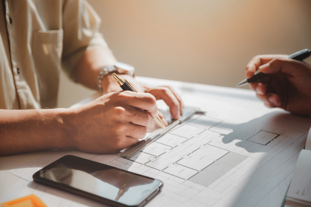Architects discussing floor plans with pens and smartphone on desk.