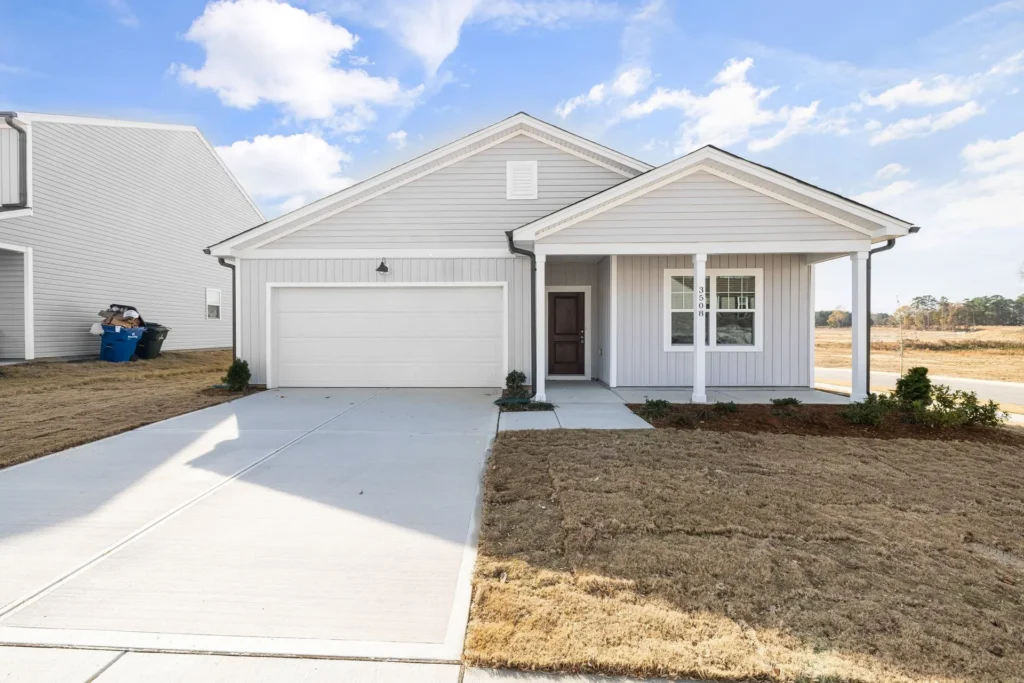 Single-story gray house with two-car garage, porch, and manicured lawn under a clear blue sky.